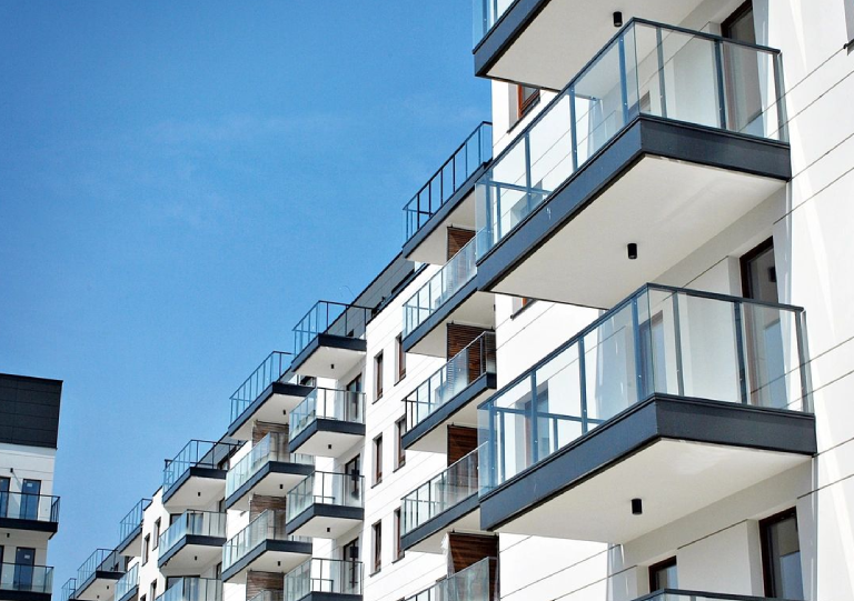 Modern apartment building with glass balconies under clear blue sky.