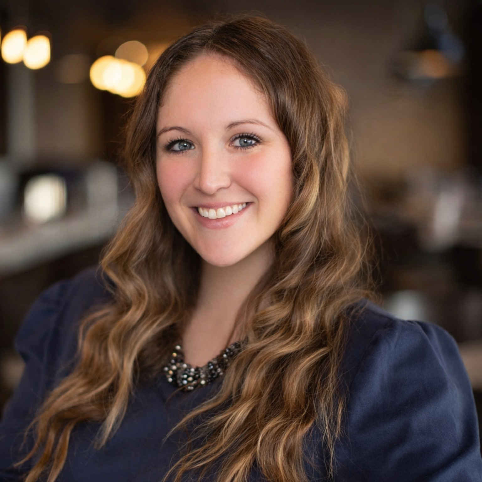 Smiling woman with long wavy hair in a cozy indoor setting.